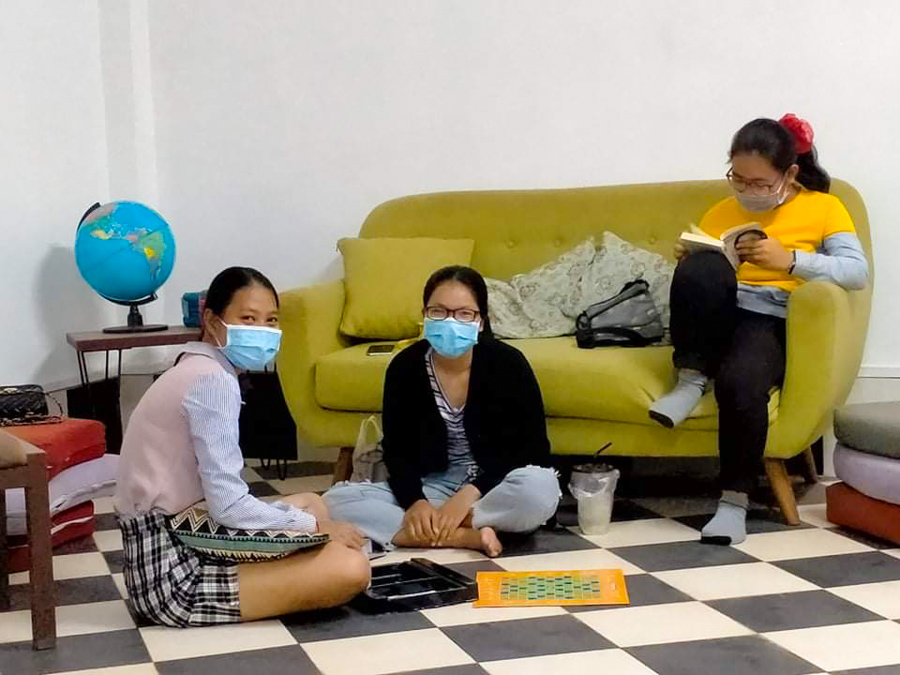 Three young Cambodian women hanging out, playing board games and reading